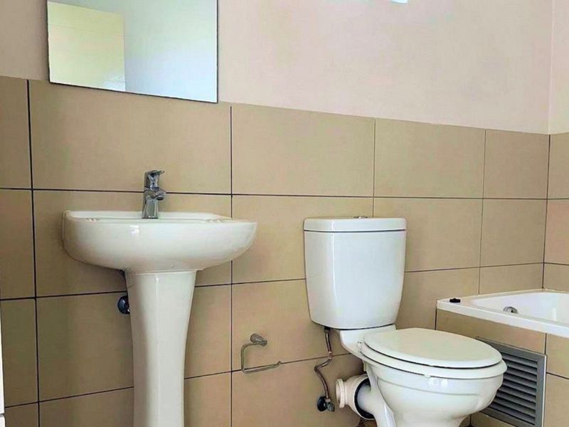A functional bathroom featuring a pedestal basin, toilet, and bathtub with neutral wall tiling.