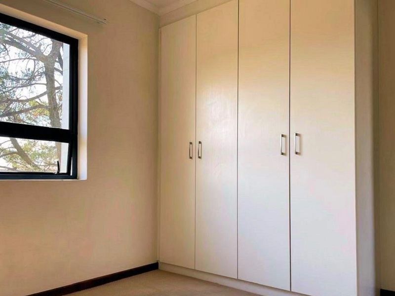 A clean, empty bedroom featuring neutral walls, carpeted flooring, and floor-to-ceiling built-in cupboards with modern hardware.