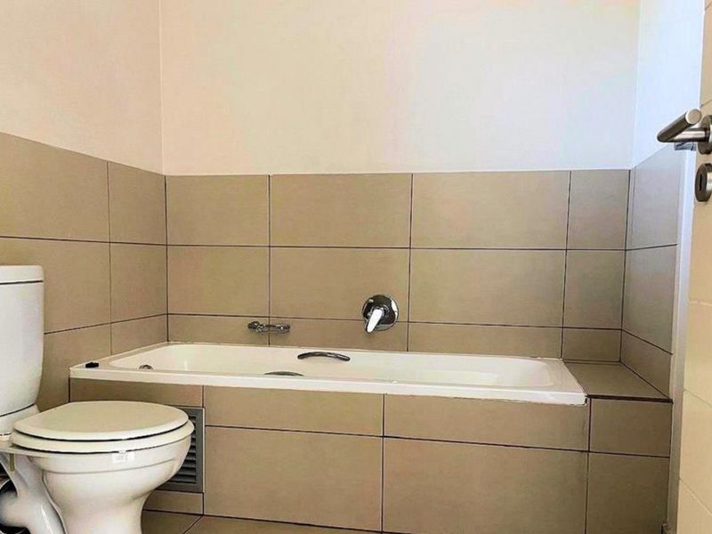 A clean, neutral-toned bathroom featuring a built-in bathtub, tiled walls, and a standard toilet suite.
