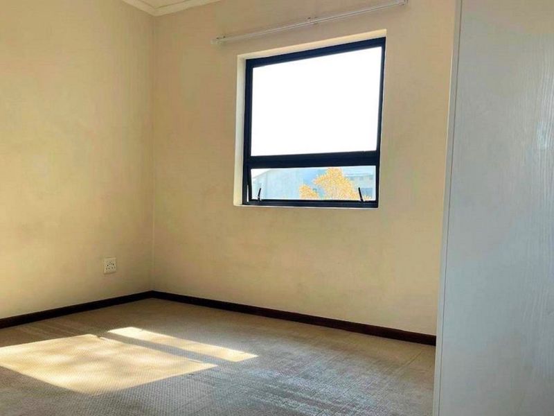 A bright, empty bedroom featuring neutral walls, carpeted flooring, and a built-in cupboard, offering a clean canvas for personalization.