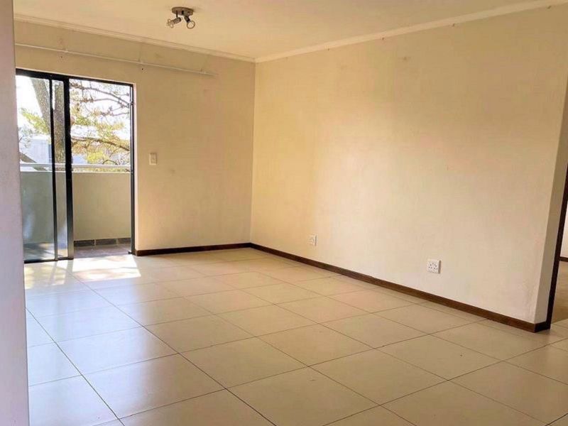 An empty, open-plan living area featuring neutral tiled flooring and a sliding glass door providing access to an outdoor balcony.
