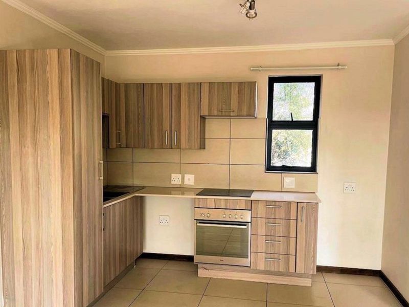 A clean, functional kitchen featuring wood-look cabinetry, built-in oven and hob, tiled splashbacks, and neutral floor tiles.