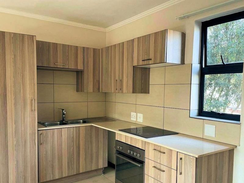 A clean, modern kitchen featuring wood-look laminate cabinetry, stone countertops, a built-in oven, electric hob, and a tiled backsplash.