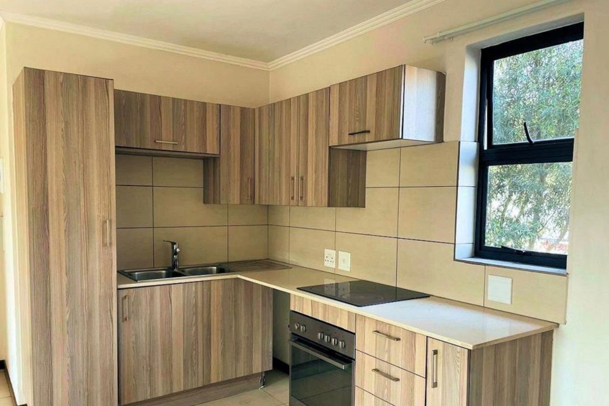 A clean, modern kitchen featuring wood-look laminate cabinetry, stone countertops, a built-in oven, electric hob, and a tiled backsplash.