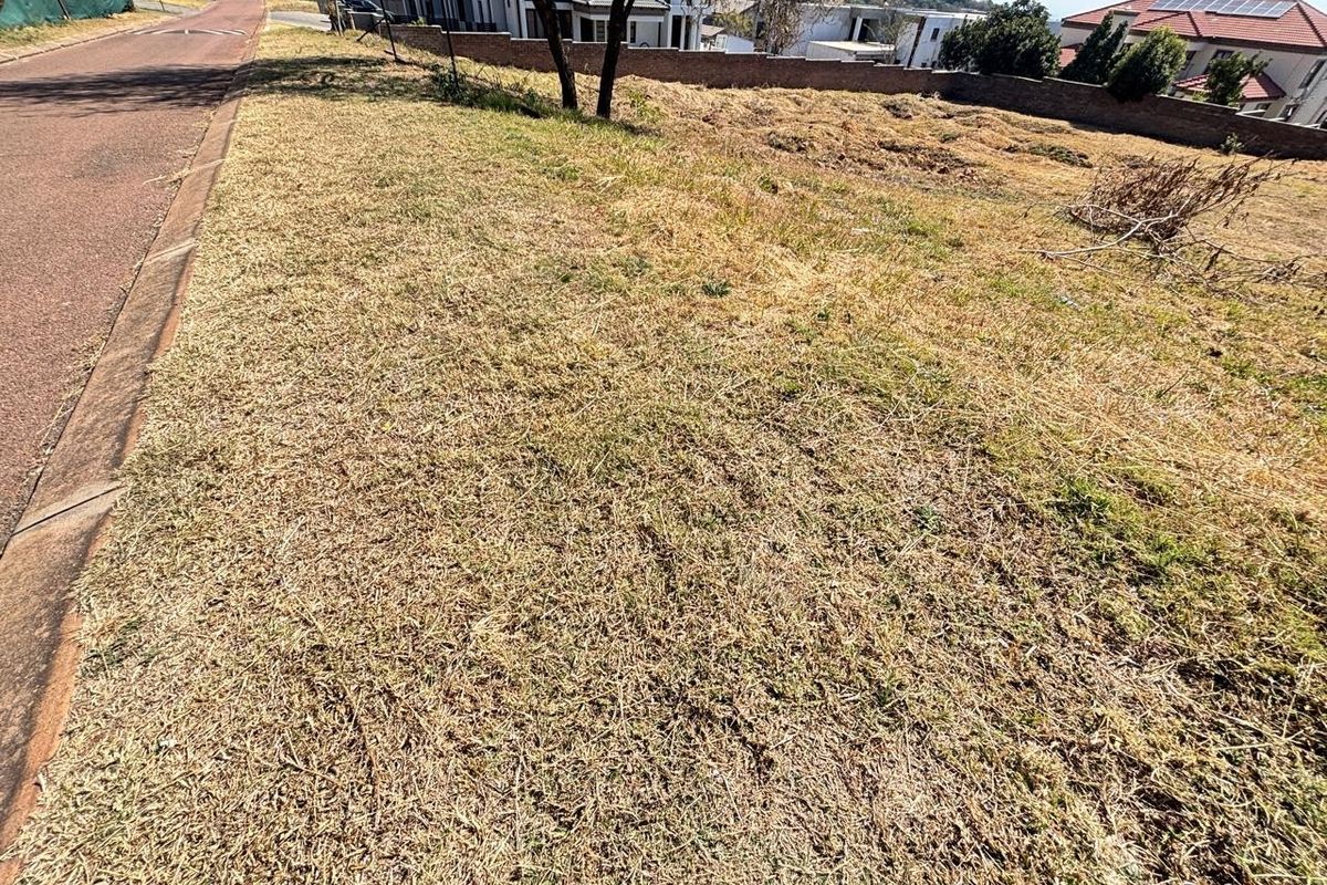 A vacant residential plot featuring a gentle slope, established boundary wall, and direct access to a paved street in a developed neighborhood.