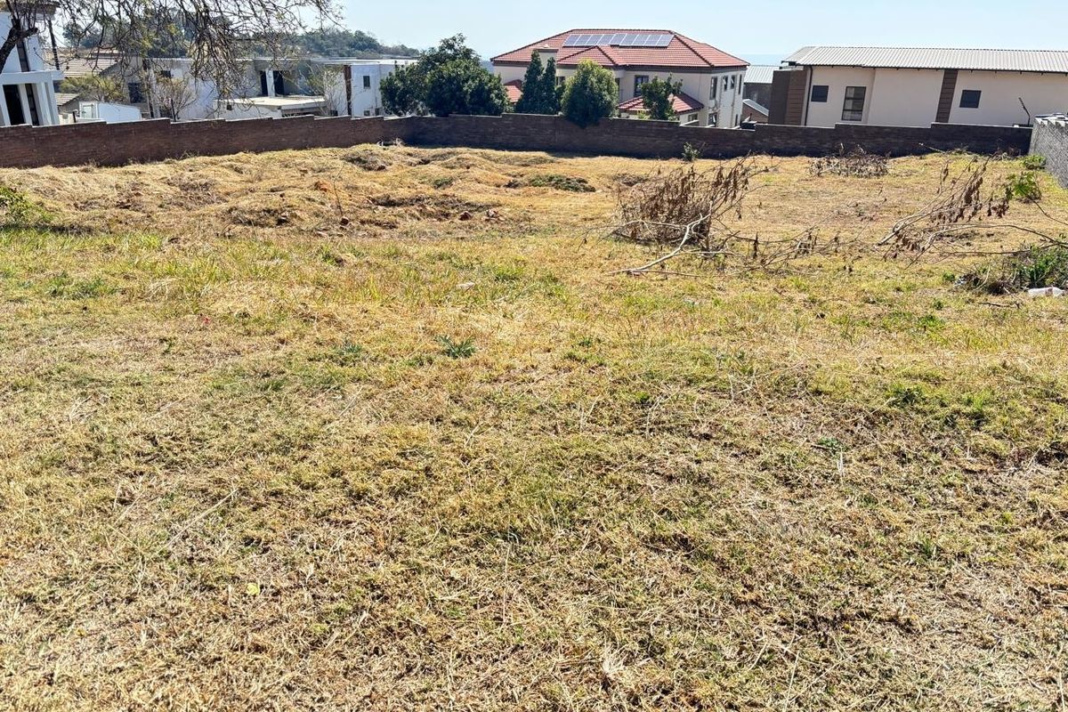 A vacant residential plot featuring a boundary wall and cleared ground, situated in a developed neighborhood.