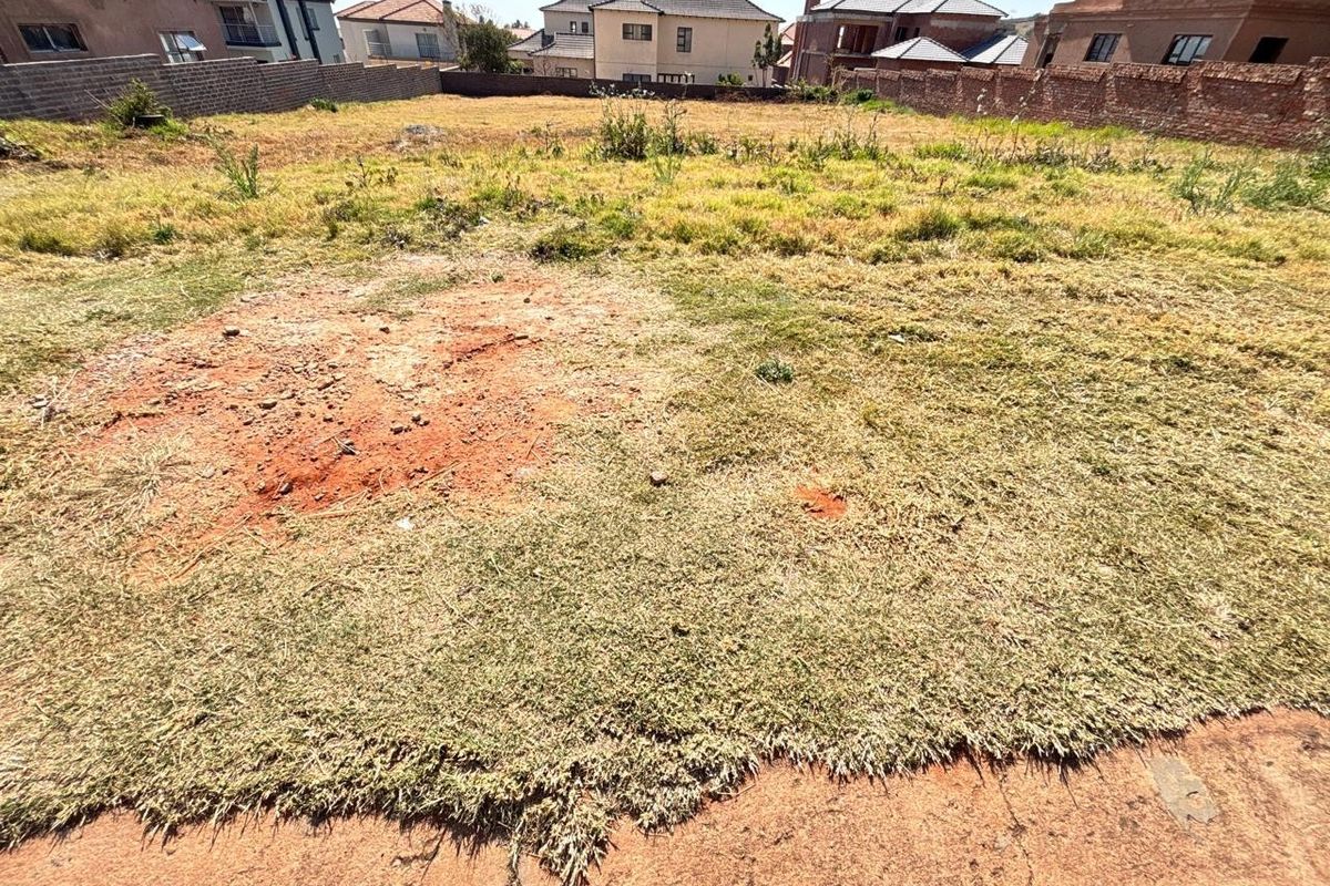 A vacant residential plot featuring perimeter brick boundary walls and an open, undeveloped grassed area.