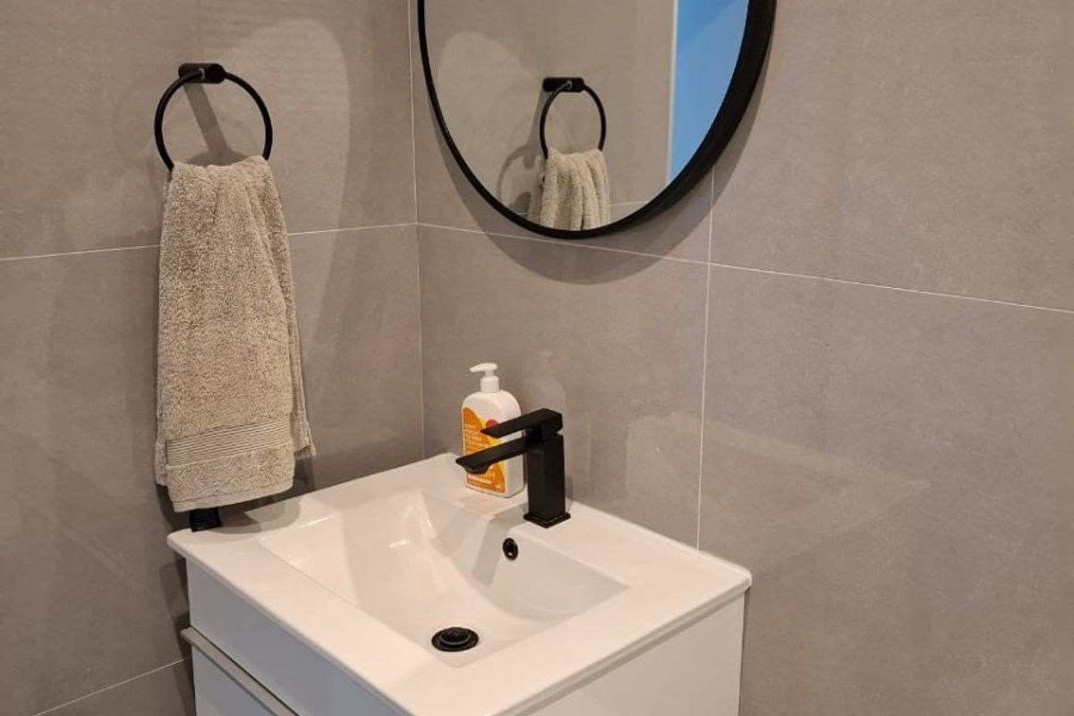 Modern bathroom featuring a sleek wall-mounted vanity, black matte fixtures, and contemporary grey porcelain wall tiling.