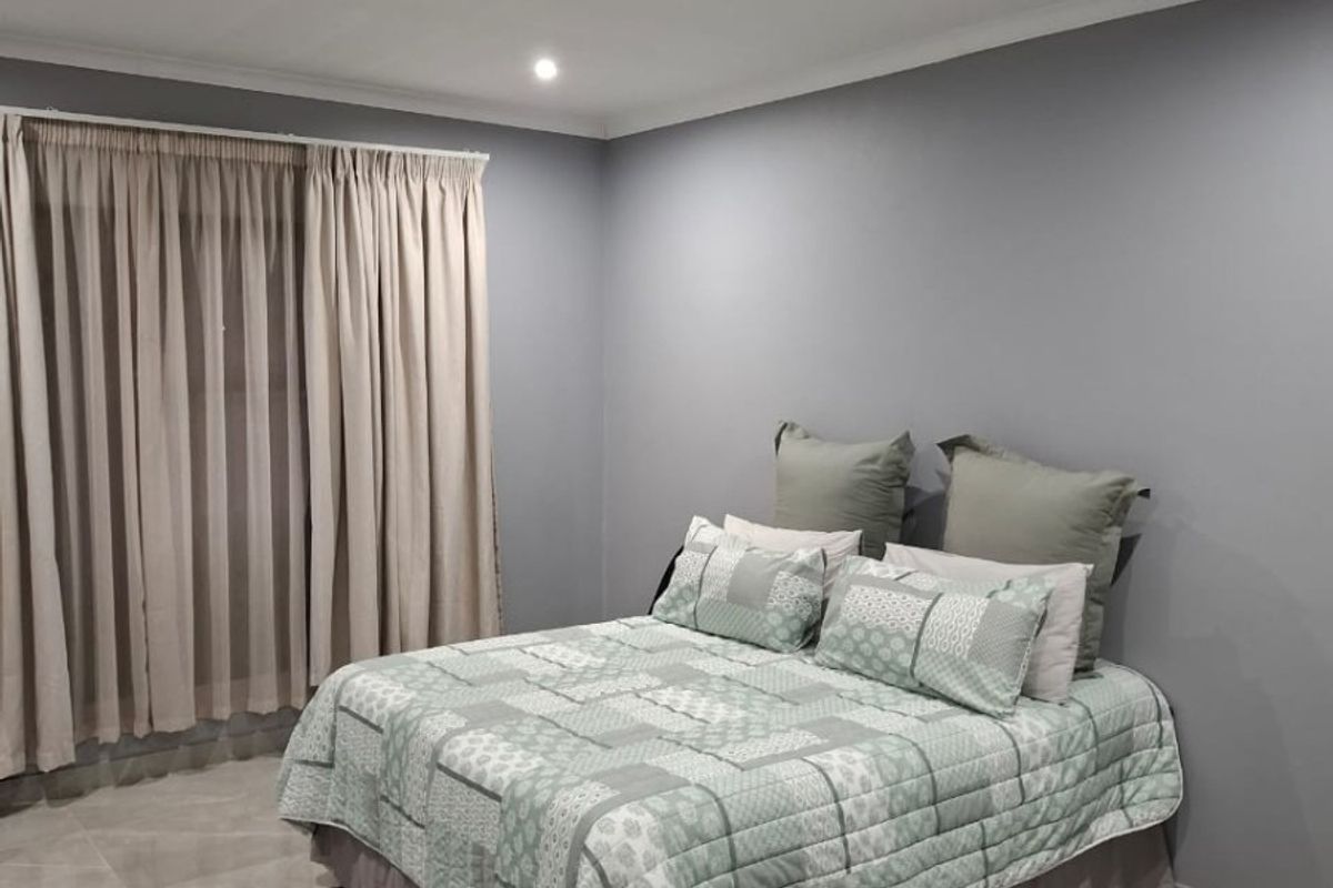 A well-maintained bedroom featuring neutral grey walls, large format floor tiles, and recessed downlighting.