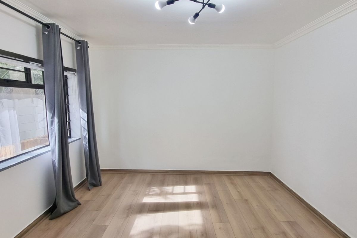 A bright, empty bedroom featuring modern laminate flooring, neutral white walls, and a contemporary ceiling light fixture.