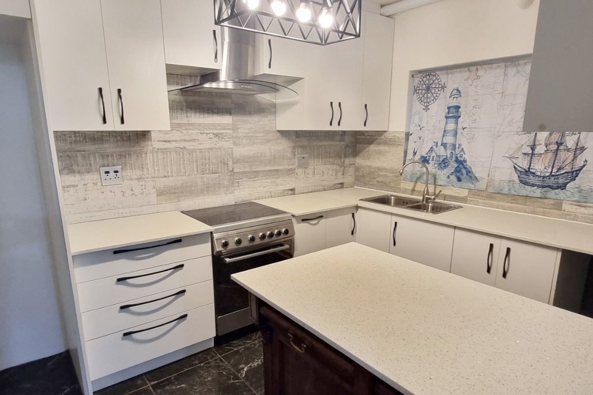 Modern kitchen featuring white cabinetry, stone countertops, a central island, and integrated stainless steel appliances, including a stove and extractor fan.