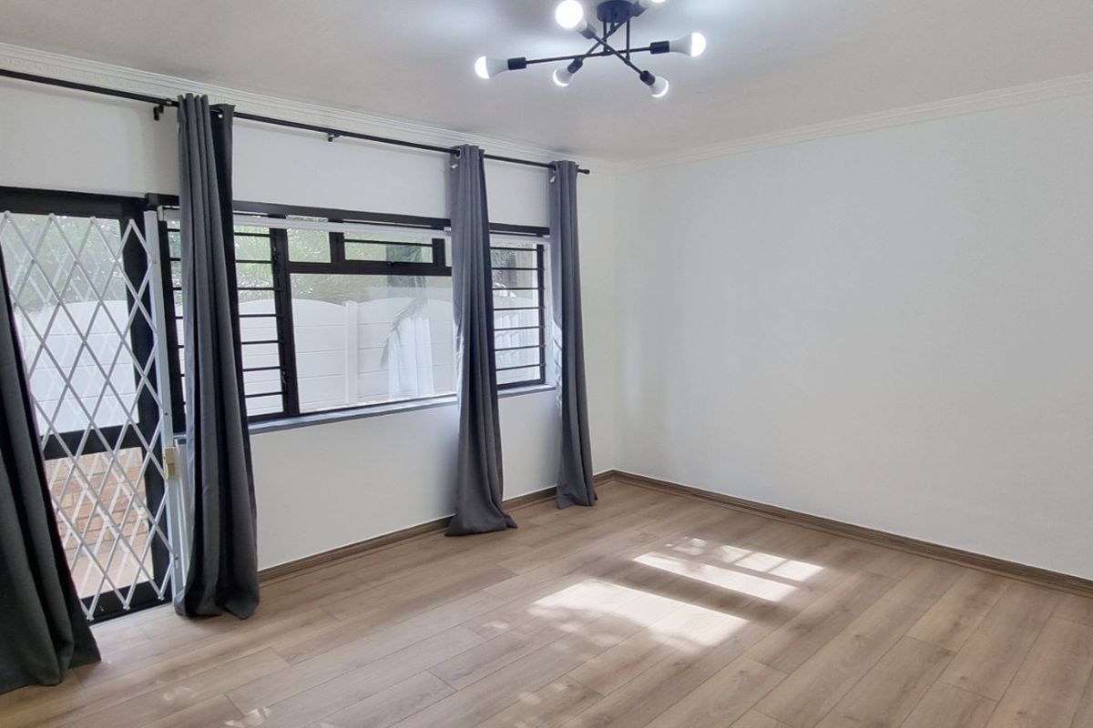 A bright, empty living room featuring laminate flooring, modern lighting, and a security gate leading to an outdoor area.