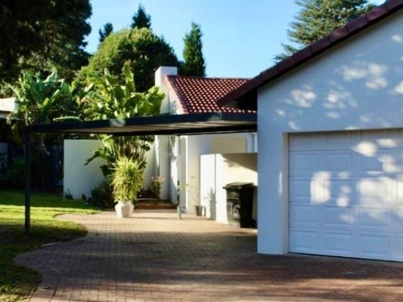 Front view of the property featuring a paved driveway, a single garage, and a covered carport area with established garden surroundings.