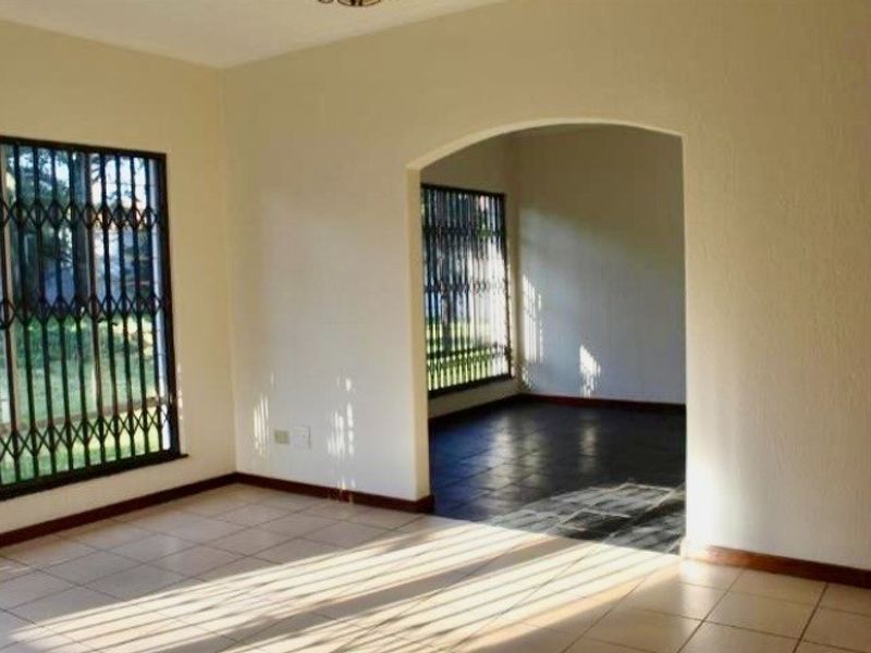 An empty living area featuring tiled flooring, an arched transition to an adjacent space, and windows fitted with security bars.