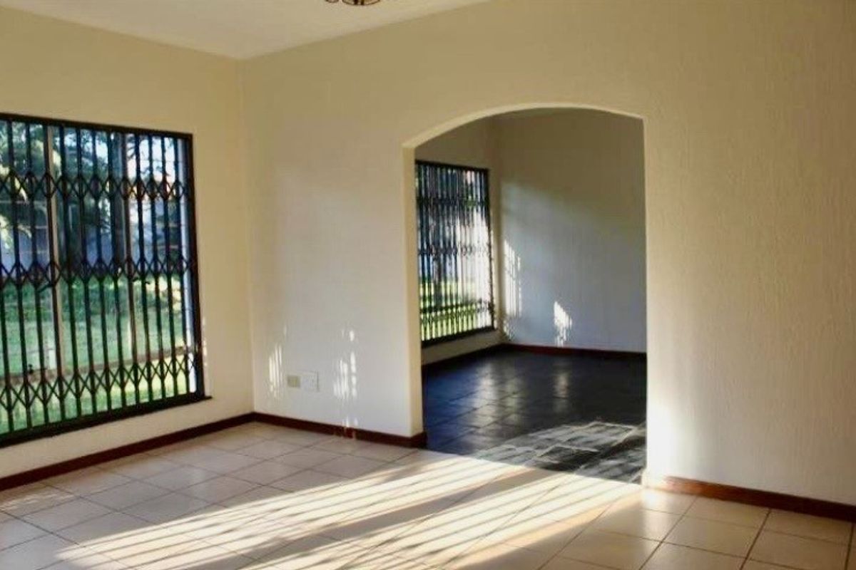 An empty living area featuring tiled flooring, an arched transition to an adjacent space, and windows fitted with security bars.