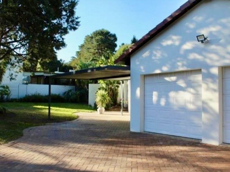 A well-maintained front exterior featuring a double garage, paved driveway, and a covered carport area set within a landscaped garden.