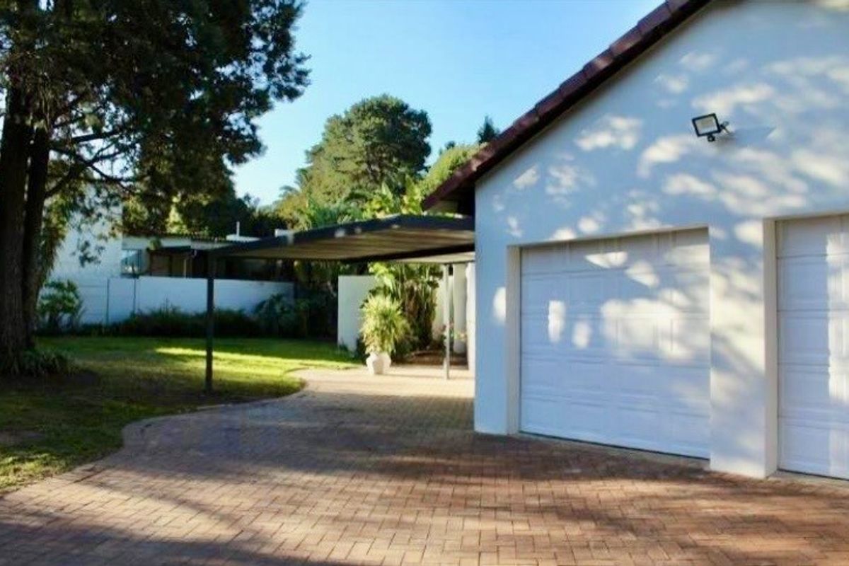 A well-maintained front exterior featuring a double garage, paved driveway, and a covered carport area set within a landscaped garden.