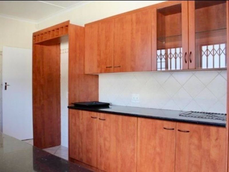 A functional kitchen featuring warm-toned laminate cabinetry, dark granite countertops, and a classic tiled backsplash with ample storage space.