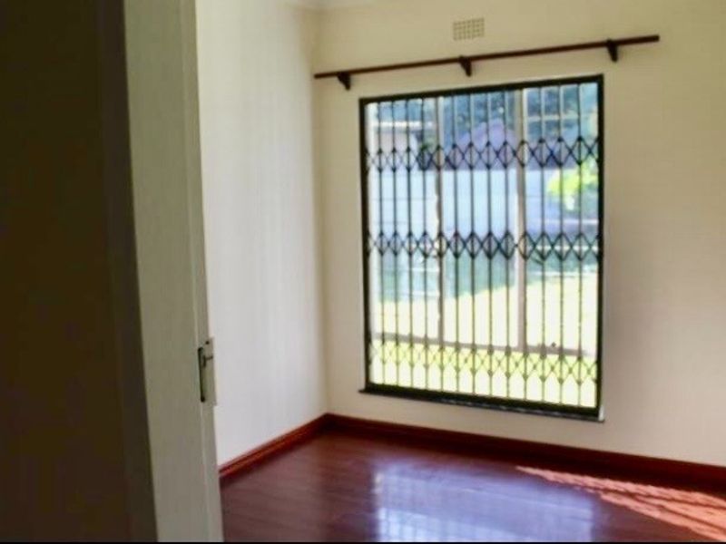 An empty bedroom featuring laminate flooring and a window fitted with a security gate.
