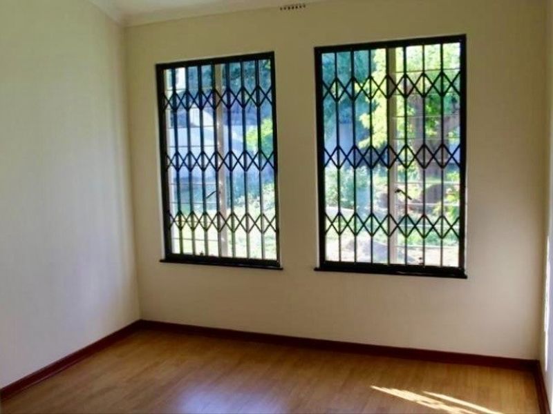 An empty bedroom featuring laminate flooring and windows fitted with security bars.