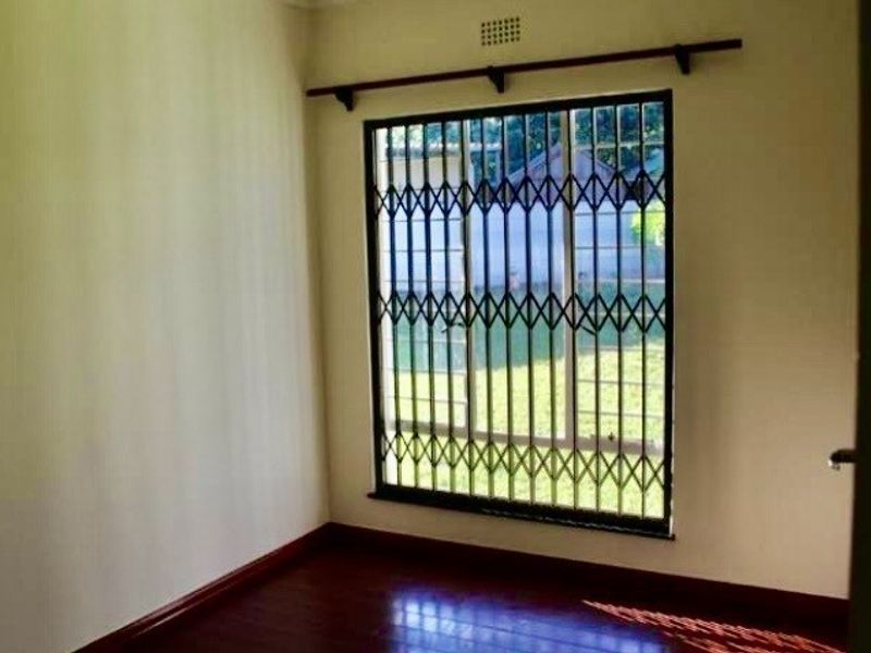 An empty bedroom featuring dark laminate flooring and a window fitted with a security gate.
