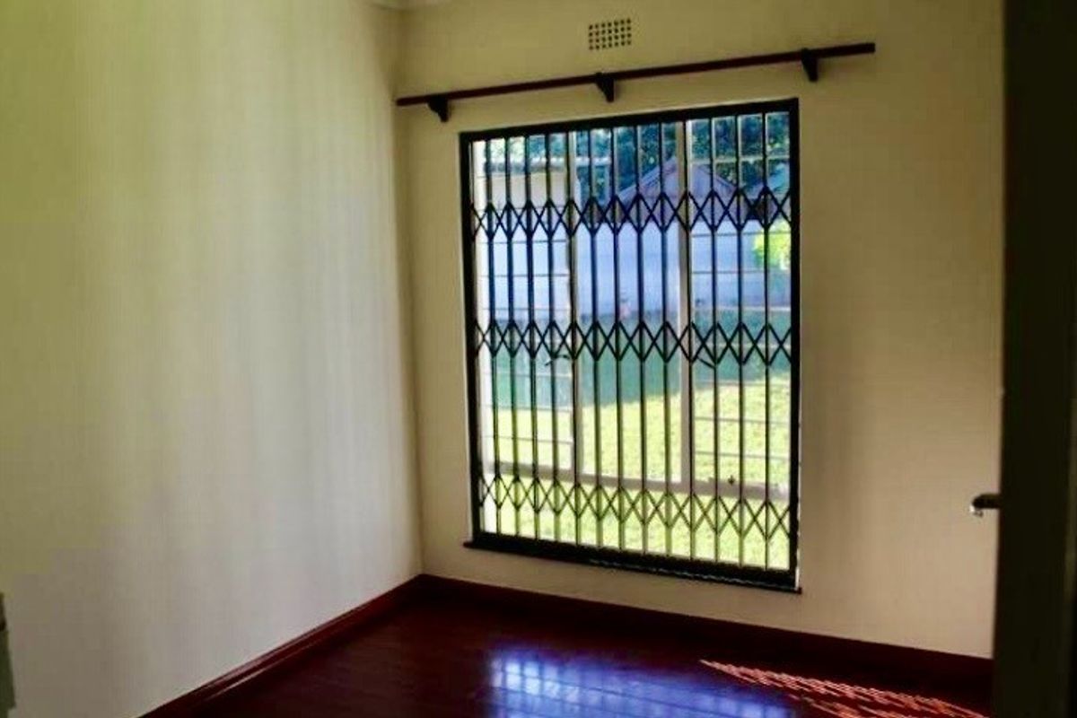An empty bedroom featuring dark laminate flooring and a window fitted with a security gate.