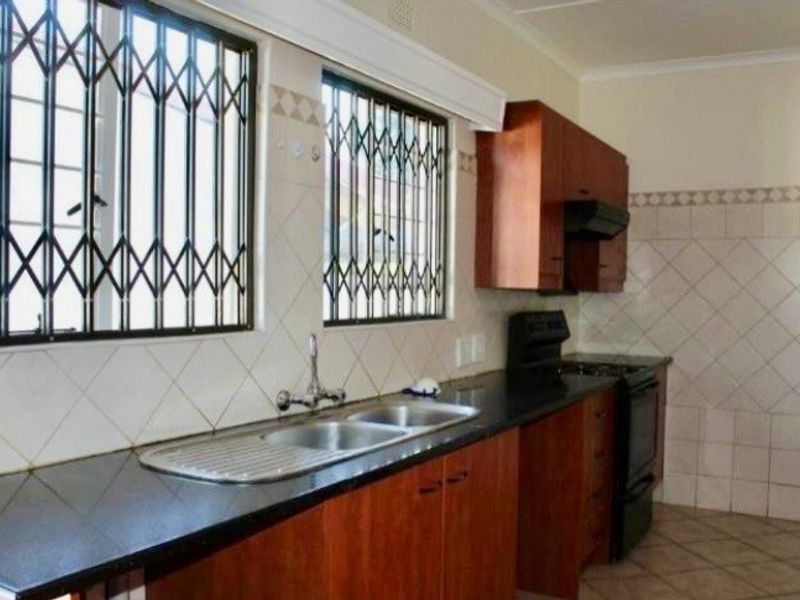 A functional kitchen featuring laminate cabinetry, dark stone countertops, a double sink, and tiled backsplash with security gates on the windows.