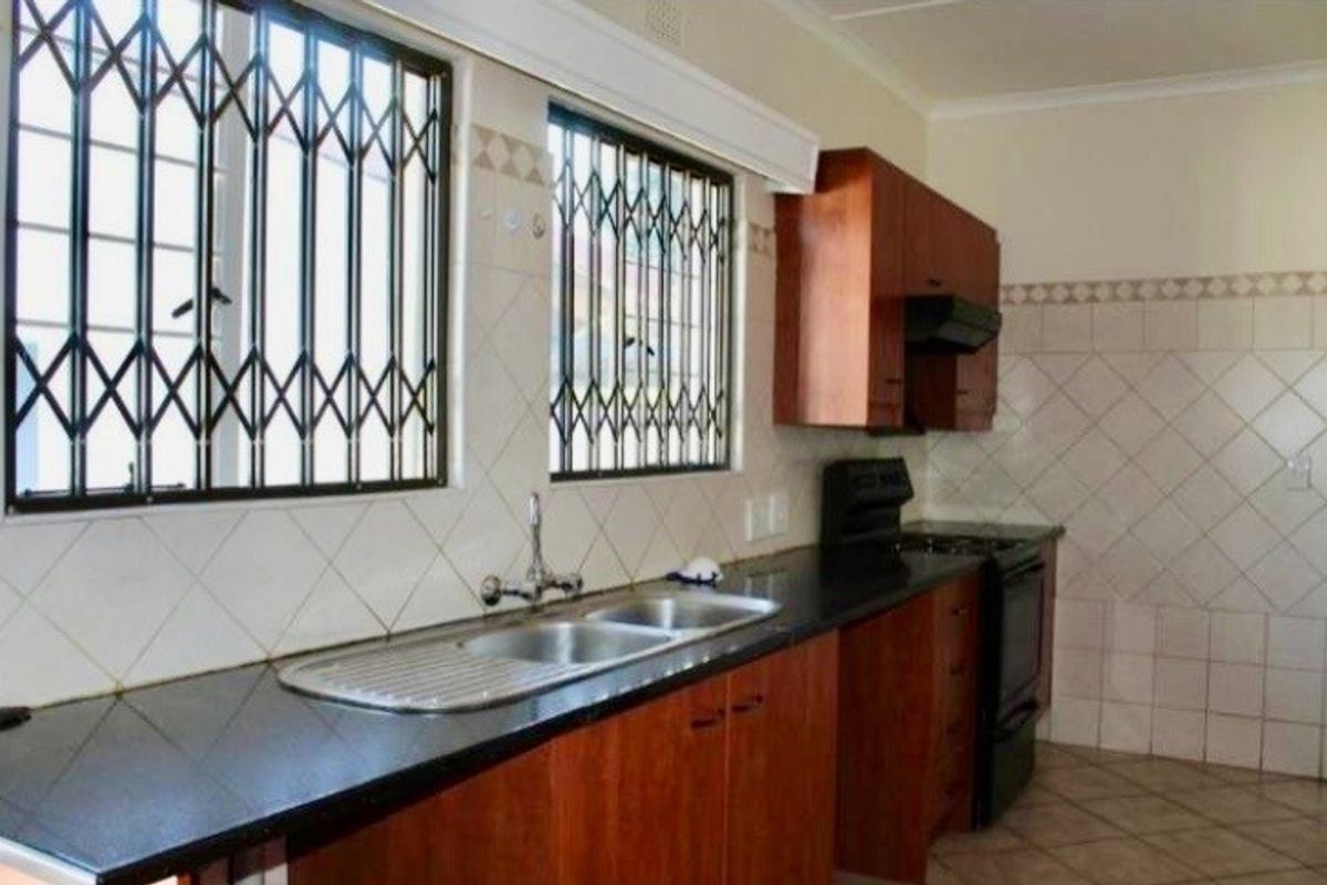 A functional kitchen featuring laminate cabinetry, dark stone countertops, a double sink, and tiled backsplash with security gates on the windows.