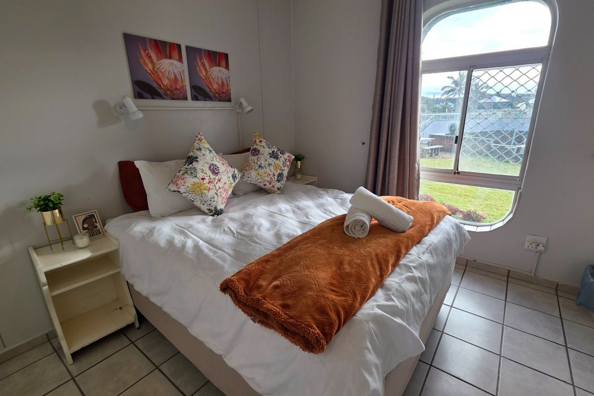 A bedroom featuring tiled flooring and an arched window with security screening, providing natural light and garden views.