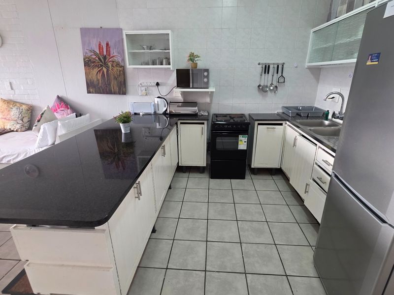 Open-plan kitchen featuring granite countertops, white cabinetry, tiled flooring, and a functional layout integrated with the living area.
