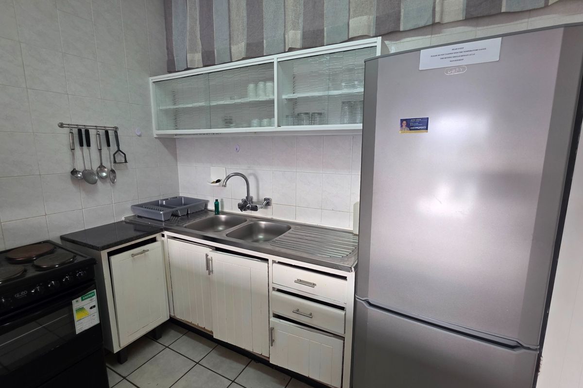 Compact kitchen featuring white cabinetry, tiled splashbacks, a double bowl stainless steel sink, and a freestanding electric stove.