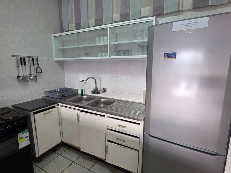 Compact kitchen featuring white cabinetry, tiled splashbacks, a double bowl stainless steel sink, and a freestanding electric stove.