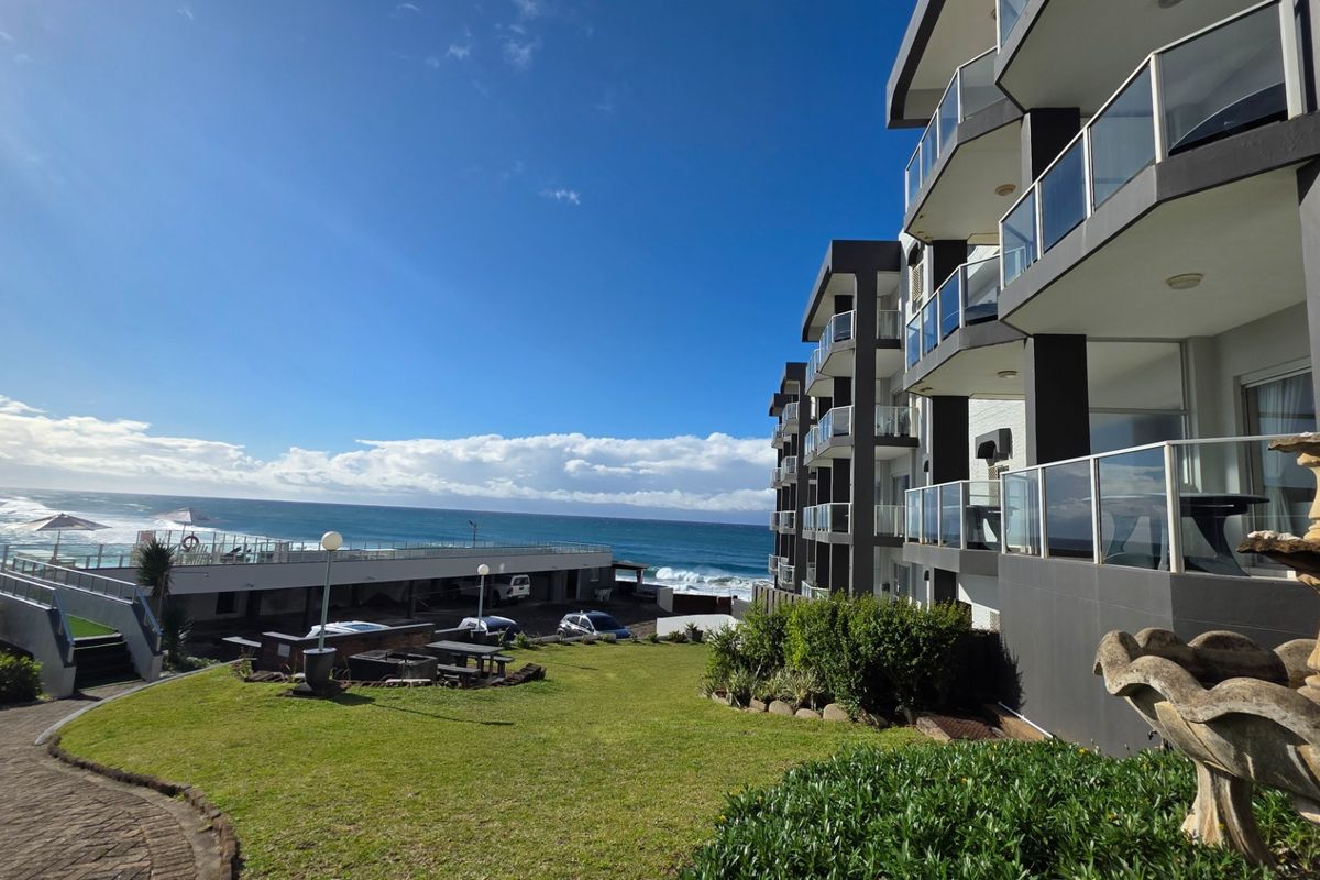 Rear view of the apartment complex featuring tiered balconies with glass balustrades, overlooking a landscaped garden and the ocean.