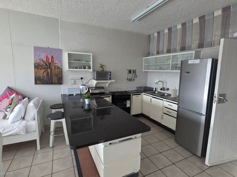 Open-plan kitchen and living area featuring a granite-topped island, built-in cabinetry, and tiled flooring, offering a functional layout for modern apartment living.