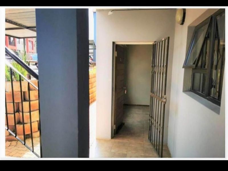An exterior view of an apartment entrance featuring a security gate, tiled flooring, and a top-hung window.