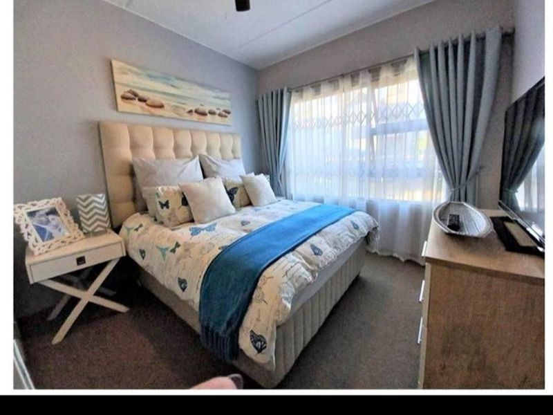 A cozy bedroom featuring neutral wall tones, carpeted flooring, and a window fitted with a security gate and curtains.