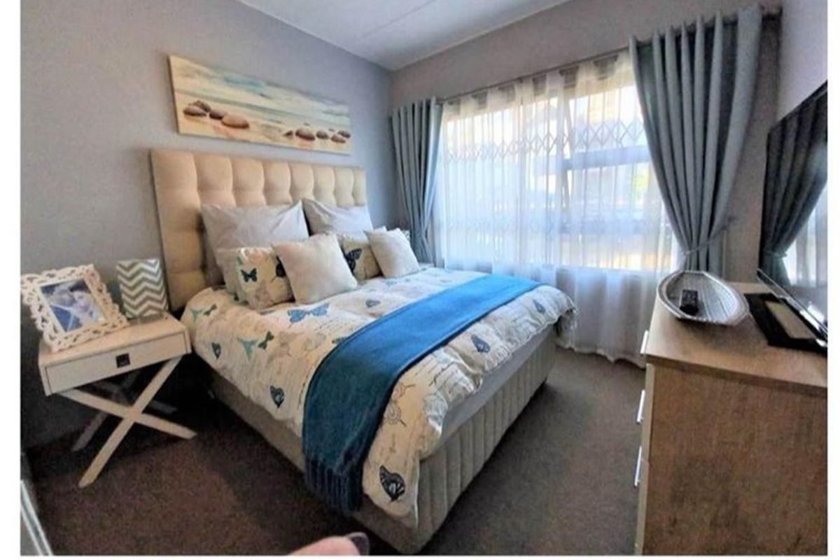 A cozy bedroom featuring neutral wall tones, carpeted flooring, and a window fitted with a security gate and curtains.