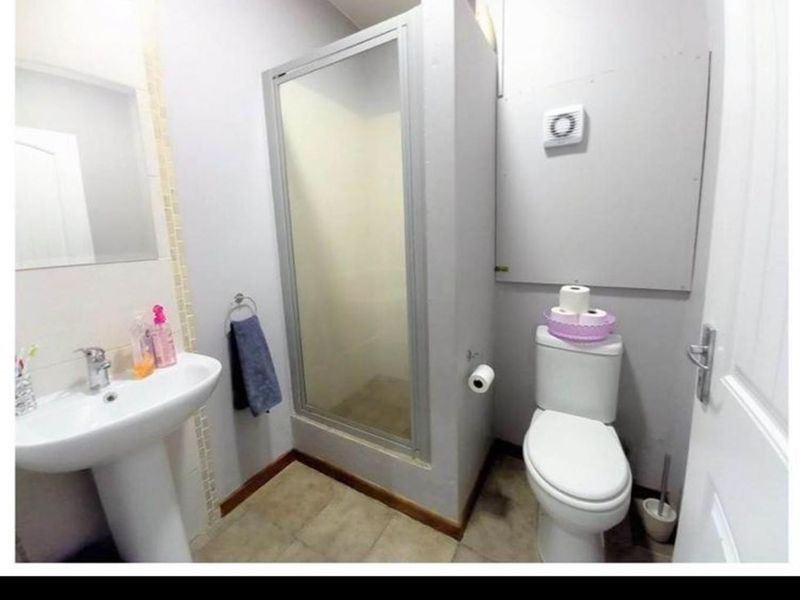 Compact bathroom featuring a pedestal basin, enclosed shower, and toilet, with neutral wall finishes and tiled flooring.