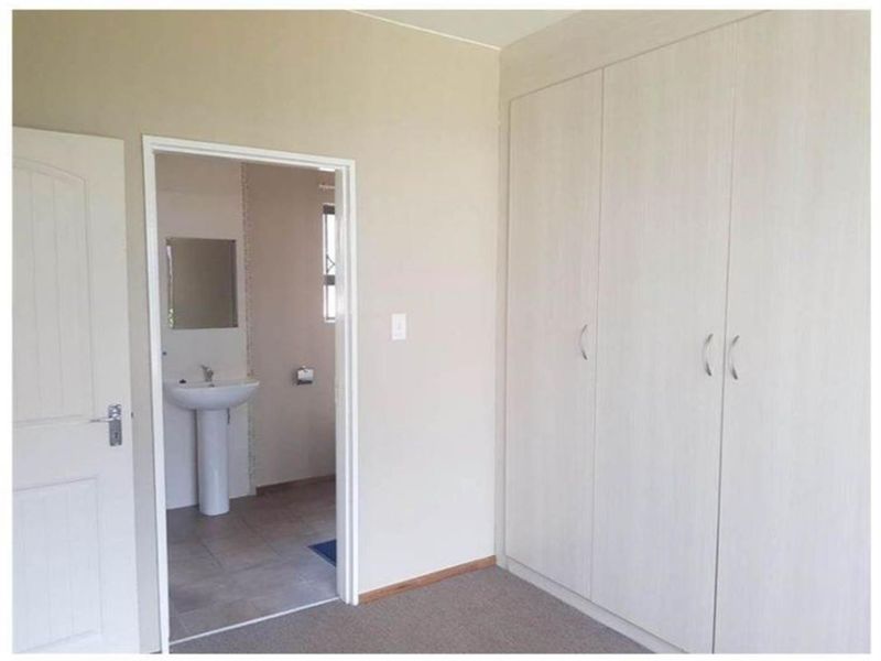 A bedroom featuring built-in cupboards and carpeted flooring, with an adjoining bathroom visible through the doorway containing a pedestal basin.