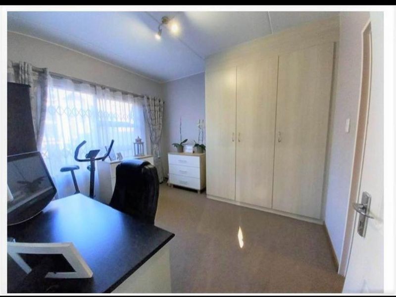 A bedroom featuring neutral-toned built-in cupboards, carpeted flooring, and a window fitted with a security gate.