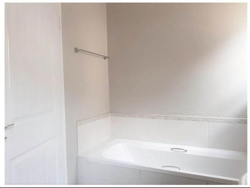 A clean, neutral bathroom featuring a built-in bathtub with a tiled splashback and a wall-mounted towel rail.