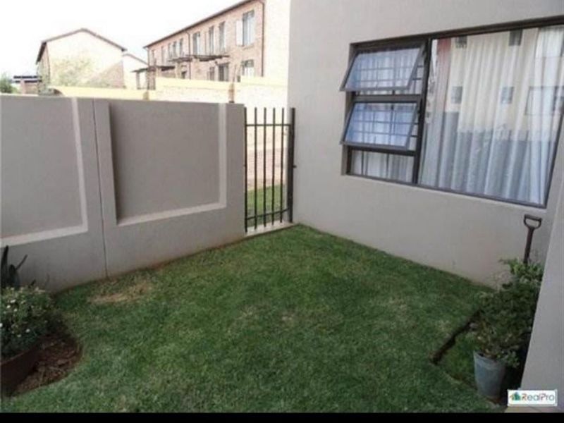 A private rear garden area featuring a small lawn, boundary wall, and metal access gate, adjacent to the apartment building.