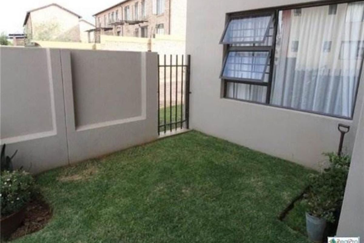A private rear garden area featuring a small lawn, boundary wall, and metal access gate, adjacent to the apartment building.