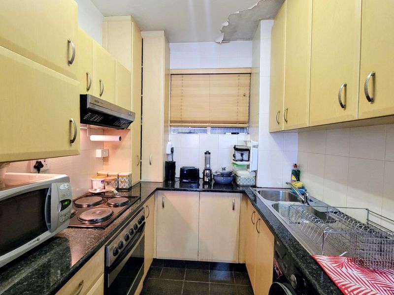 Compact galley-style kitchen featuring laminate cabinetry, granite countertops, and integrated appliances, currently showing signs of ceiling water damage requiring repair.