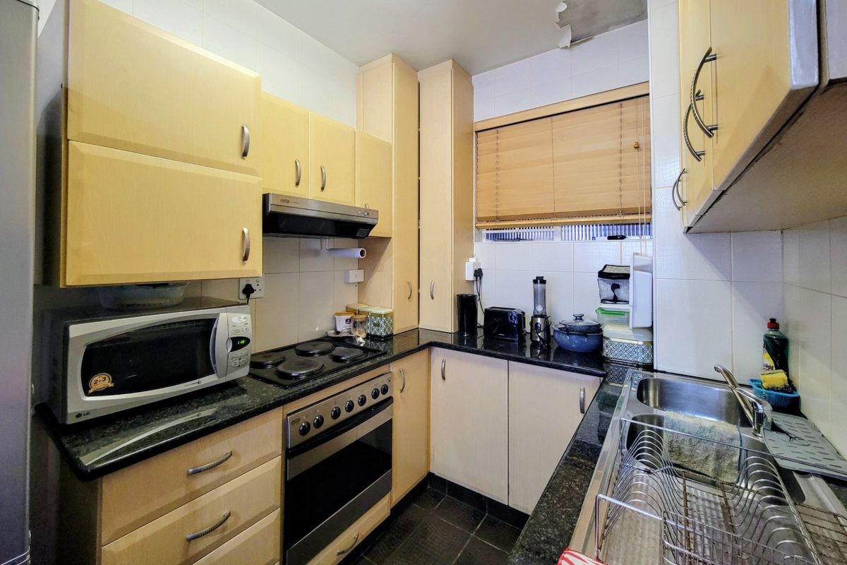 Compact kitchen featuring light wood cabinetry, granite countertops, built-in oven, electric hob, and a double stainless steel sink.