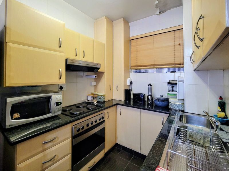 Compact kitchen featuring light wood cabinetry, granite countertops, built-in oven, electric hob, and a double stainless steel sink.