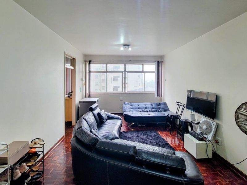 A living room featuring traditional parquet flooring and a large window providing natural light.