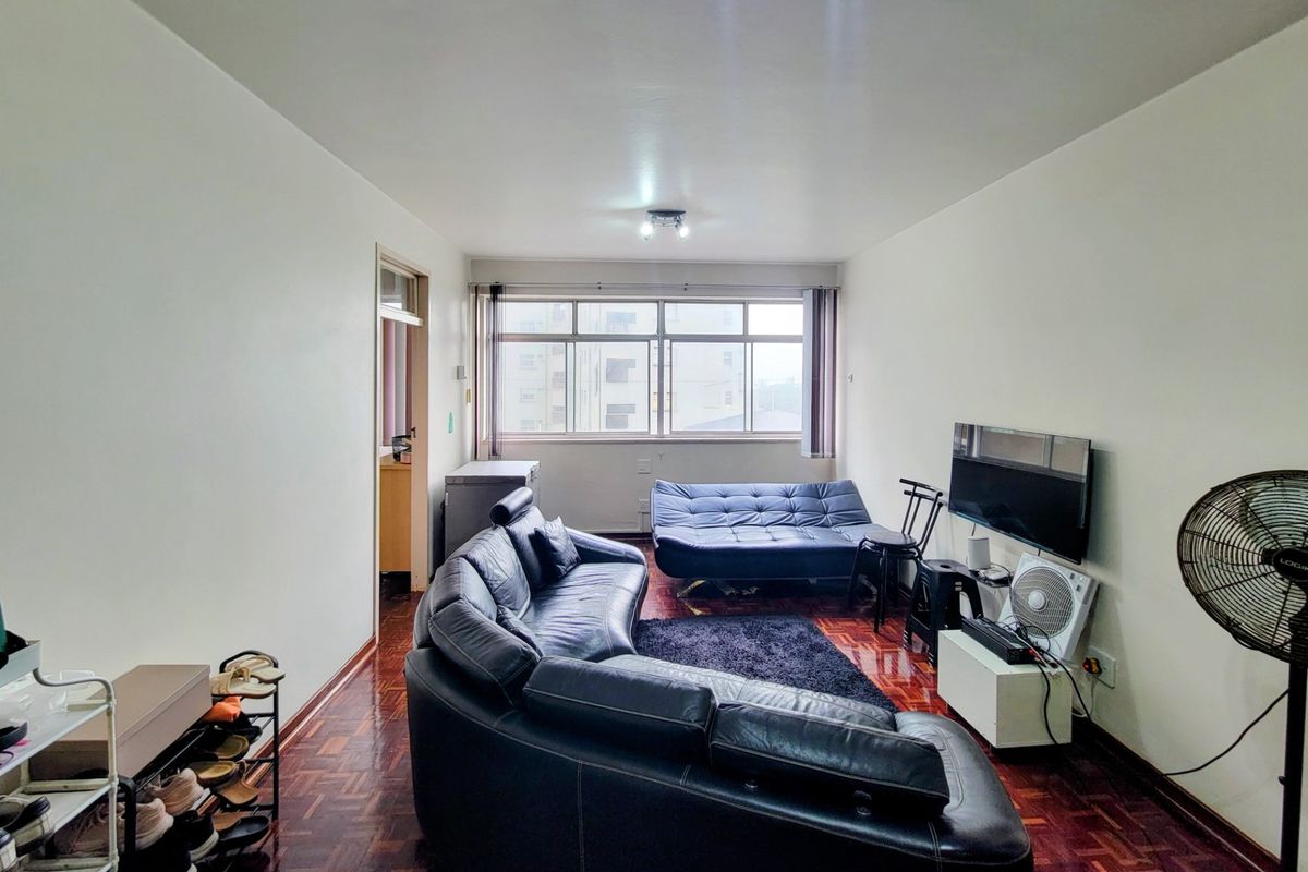 A living room featuring traditional parquet flooring and a large window providing natural light.