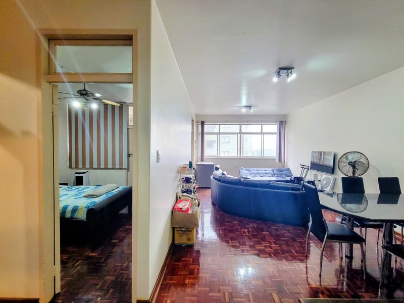 Open-plan living and dining area featuring traditional parquet flooring and large windows, with an adjacent bedroom visible through the doorway.