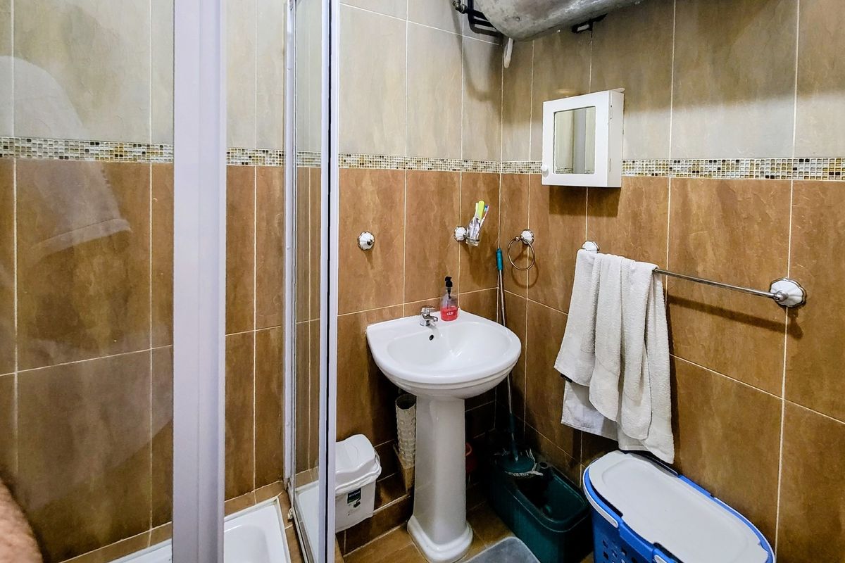 Compact bathroom featuring a pedestal basin, shower enclosure, and full-height wall tiling. The space includes a wall-mounted medicine cabinet and functional towel rail.